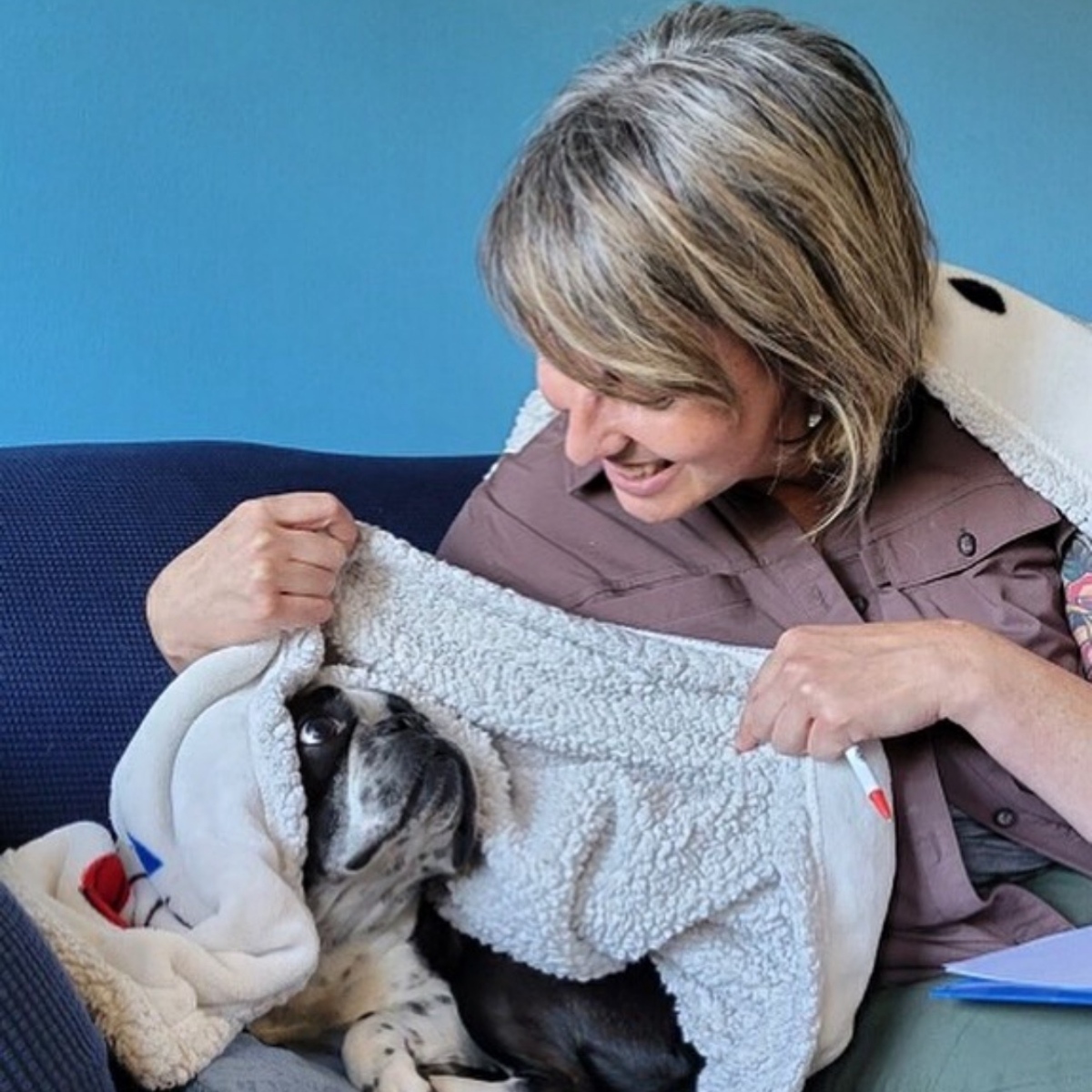 A woman lovingly holds a dog swaddled in a soft blanket