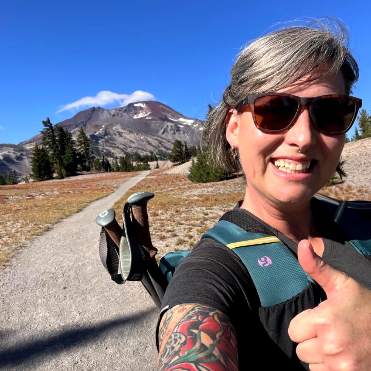 A woman with tattoos and a backpack stands confidently